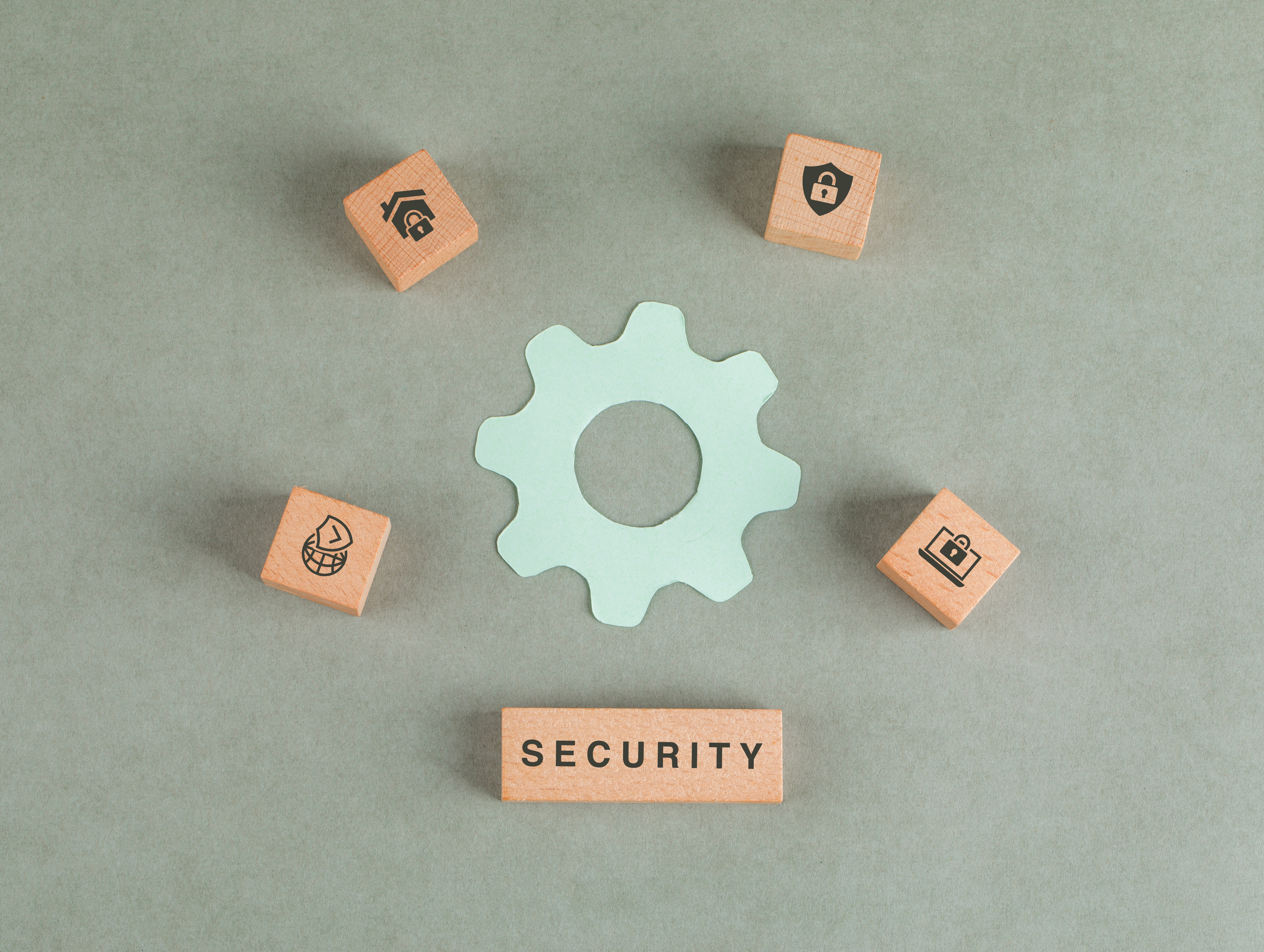 Wooden blocks with security icons surround a green gear on a gray background. A block with 
