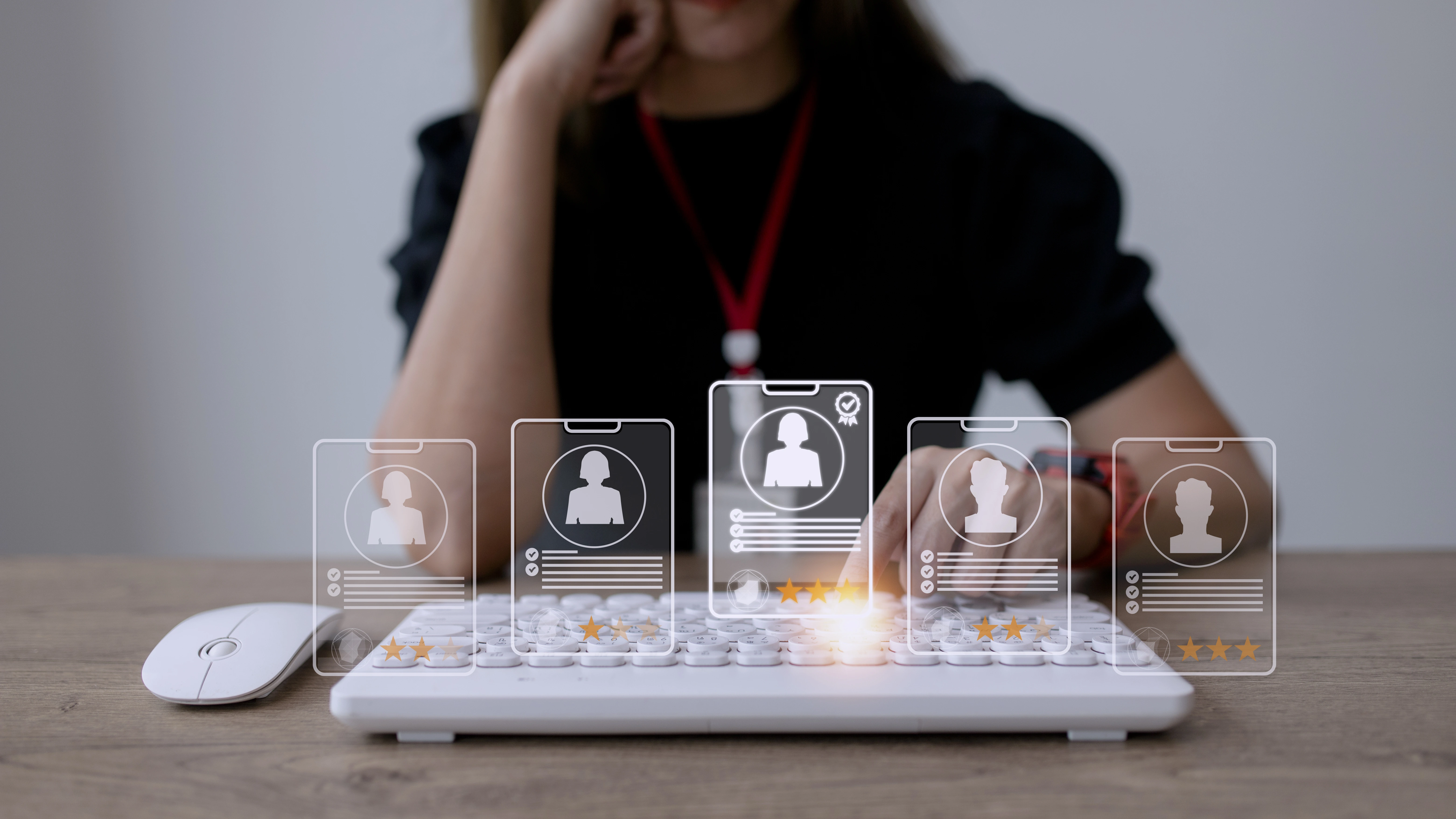 Person typing on keyboard with transparent profile icons hovering above. Icons show silhouettes, stars. Office setting, focused mood.