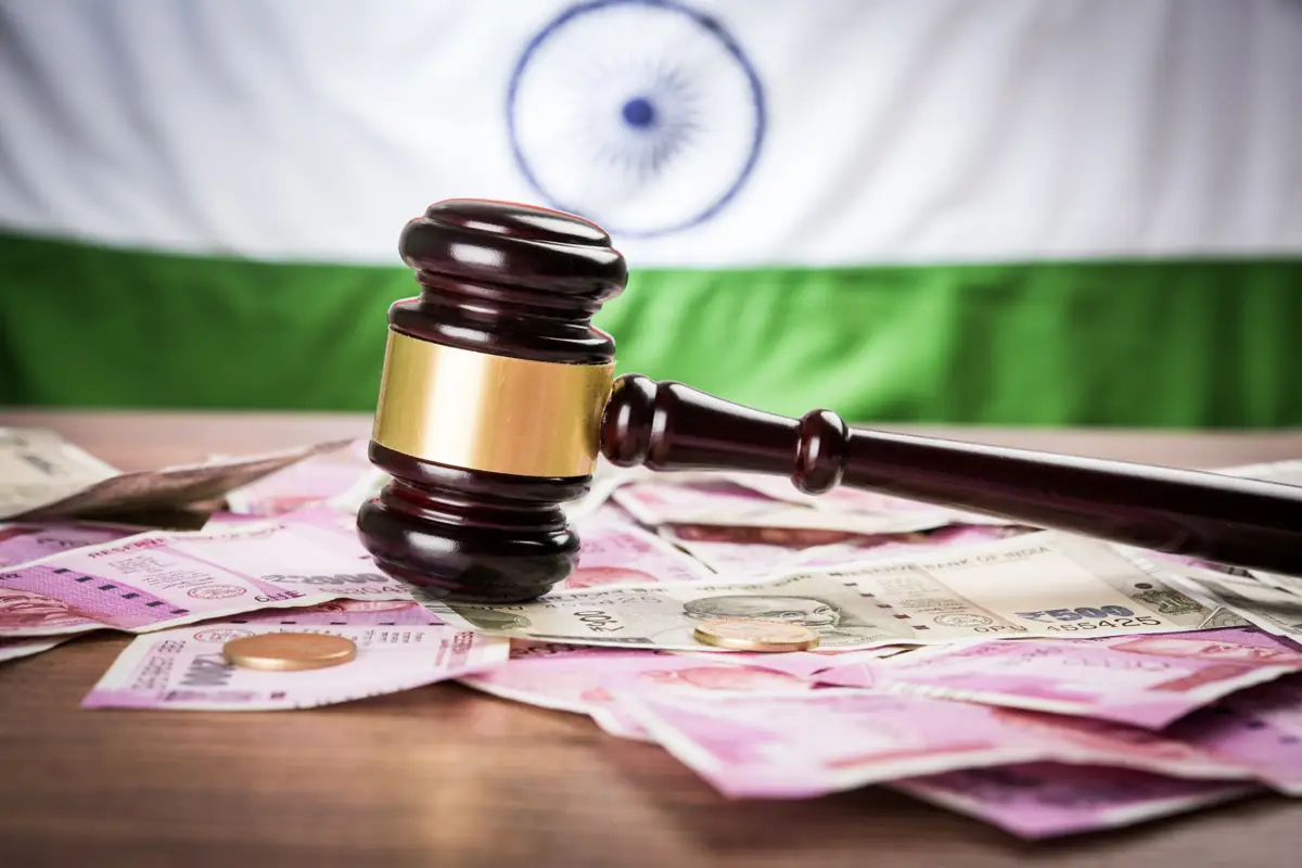 Gavel on scattered Indian rupee notes with the Indian flag in the background, highlighting themes of law and finance.